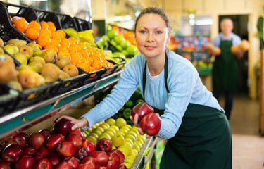 friendly woman seller chooses ripe and juicy apples for buyer