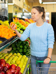 Obraz premium in large supermarket with wide assortment, woman buys tangerines