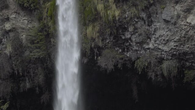 waterfall falling into dark cave entrance, early evening