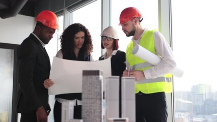 Focus on city model, multicultural workers reading blueprint. Architects, designers and engineers working on a building complex prototype project of residential or business district.