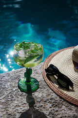cold mojito cocktail with limes at the pool with black sunglasses and straw hat