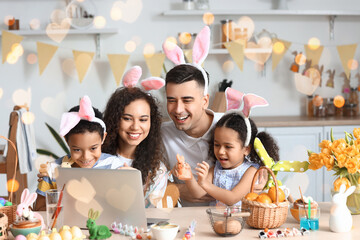 Happy interracial family in bunny ears using laptop in kitchen on Easter day