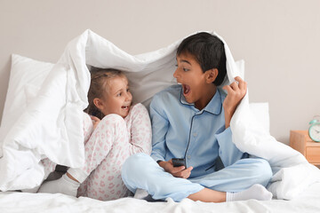 Fototapeta premium Shocked little boy and his sister watching cartoons on TV in bedroom