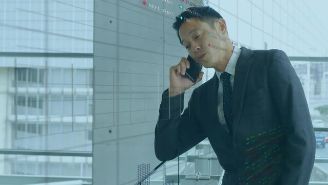 Animation of stock market data processing over asian businessman talking on smartphone at office