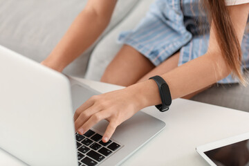 Fototapeta premium Little girl with smartwatch using laptop at home, closeup
