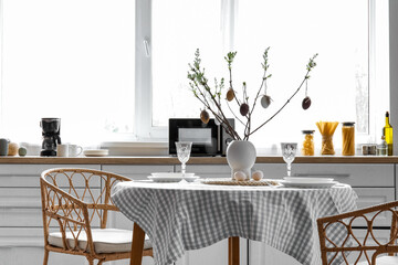 Vase with tree branches and Easter eggs on dining table in kitchen