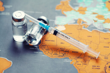 Medical syringe with a needle and a bollte with vaccine on world map.