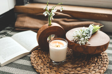 Burning candle and beautiful flowers on wooden table indoors - obrazy, fototapety, plakaty