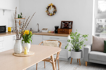 Vases with tulips, willow branches and Easter rabbit on dining table in kitchen
