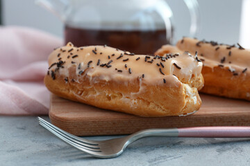 Board with delicious eclairs and fork on grey table