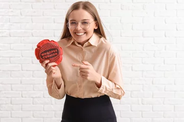 Deurstickers Young woman pointing at whoopee cushion on white brick background. April Fools' Day celebration © Pixel-Shot