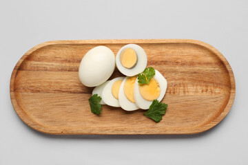 Board with slices of delicious boiled eggs and parsley on grey background