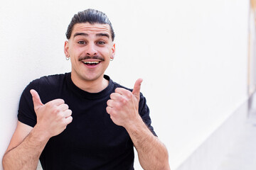 Naklejka premium young cool man smiling joyfully and looking happy, feeling carefree and positive with both thumbs up