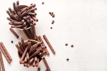 Bowls with delicious chocolate wafer rolls and coffee beans on white background