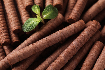 Delicious chocolate wafer rolls and mint as background, closeup