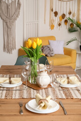 Table setting for International Women's Day celebration with tulip flowers and teapot in interior of room