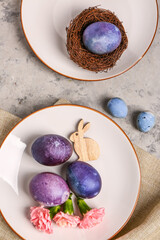 Plates with painted Easter eggs, bunny and carnation flowers on grey grunge background