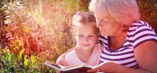 Grandmother reading to her granddaughter child book outdoors. Happy family concept