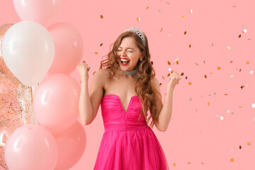 Obraz na płótnie Canvas Happy young woman in prom dress with balloons and confetti on pink background