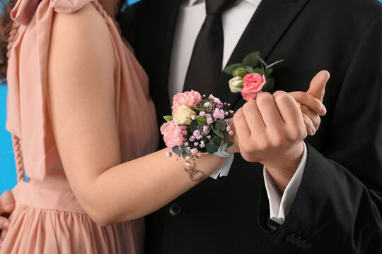 Young woman with corsage and her prom date dancing on blue background, closeup