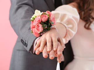 Young woman with corsage and her prom date holding hands on pink background, closeup