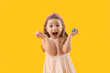 Surprised little girl with Easter eggs on yellow background