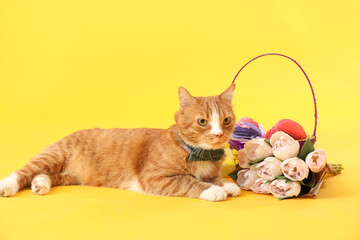 Fototapeta na wymiar Cute cat, basket with Easter eggs, gifts and tulips on yellow background