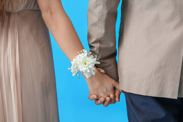 Young guy and his prom date with corsage holding hands on blue background, closeup