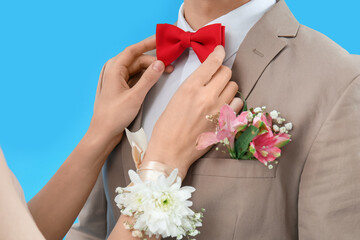 Young girl fixing bowtie of her prom date on blue background, closeup