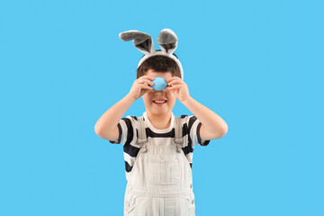 Cute little boy with bunny ears and Easter egg on light blue background