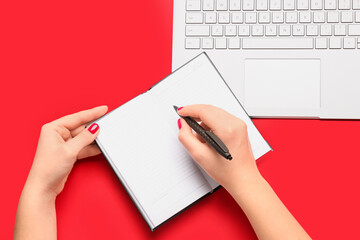 Female hands with notebook, pen and laptop on red background