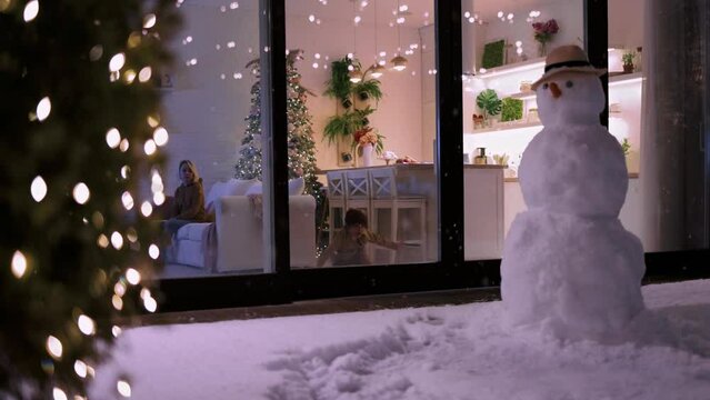 kids having fun at home, with snowflakes falling outdoors in winter evening at the background. Cozy, decorated apartment on Christmas holidays