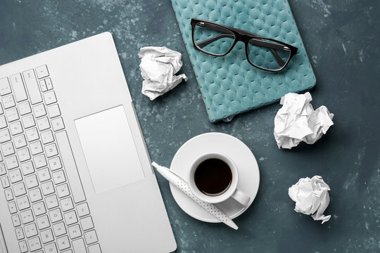 Composition with laptop, notebook, cup of coffee and crumpled paper balls on dark background