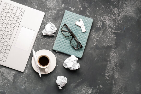 Composition with laptop, notebook, cup of coffee and crumpled paper balls on dark background
