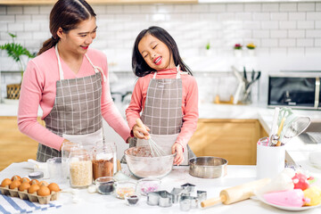 Portrait of enjoy happy love asian family mother and little toddler asian girl daughter child having fun cooking together with dough for homemade bake cookie and cake ingredient on table in kitchen