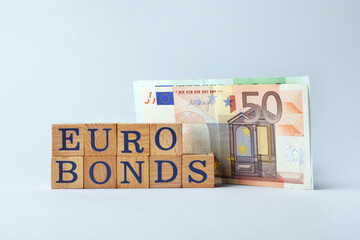 Word Eurobonds made of wooden cubes with letters and banknotes on light grey background