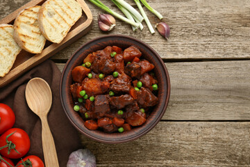 Delicious beef stew and ingredients on wooden table, flat lay. Space for text