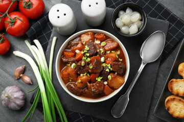 Delicious beef stew with carrots, green onions and ingredients on grey table, flat lay