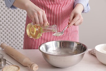 Woman pouring oil into spoon at white wooden table indoors, closeup. Cooking traditional grissini