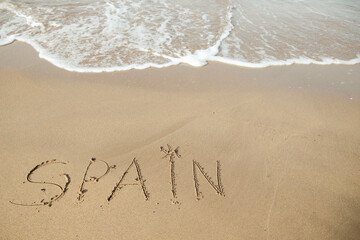 Spain lettering on the beach with wave and clear blue sea.