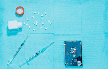 overhead view of a medical tray containing hypodermic needles, pills and a pill bottle, and a hard disk drive