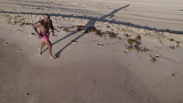 Drone orbiting footage of determinate muscular male athlete running down a shoreline on a sunny day