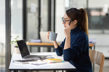 Young Asian professional business woman office worker analyst sitting at desk working on laptop thinking on project plan, analyzing marketing or financial data online, watching elearning webinar.