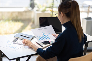 Young Asian professional business woman office worker analyst sitting at desk working on laptop thinking on project plan, analyzing marketing or financial data online, watching elearning webinar.