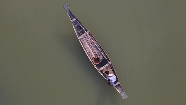 A fisherman in a wooden boat prepares baits and nets for catching fish. A bird's eye view of the dark water surface in Bangladesh from a drone.