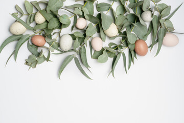 Beautiful flat lay easter composition of pastel coloured easter eggs and eucalyptus leaves on a white background, with space for copy.