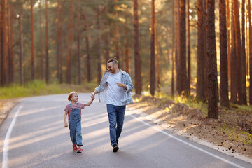 Dad and his little daughter have fun run along the forest road among tall pines. Family walk in the...