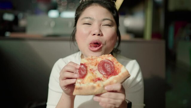 pizza lover asian woman Enjoying Pizza Holding And Biting Tasty Slice Sitting At Table while waiting for her trian at train station,Young happiness asia female have a pizza lunch break.