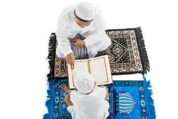 Top view of little boy learning to read the Quran with his father