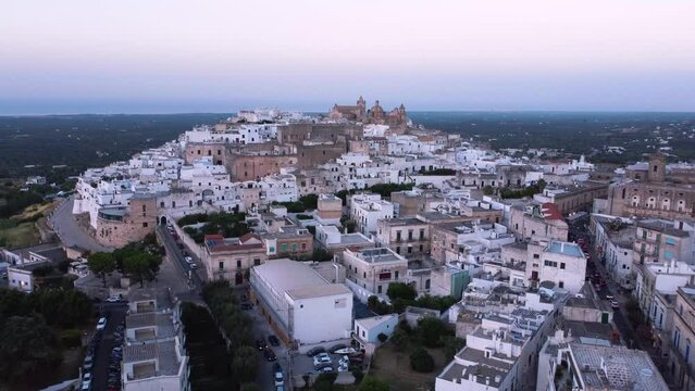 Aerial drone footage of Ostuni - La Citta Bianca (white city), Puglia, Italy at sunset. View of Cathedral, Porta Nova, the medieval historic old town landmark tourist destination from above at dusk.